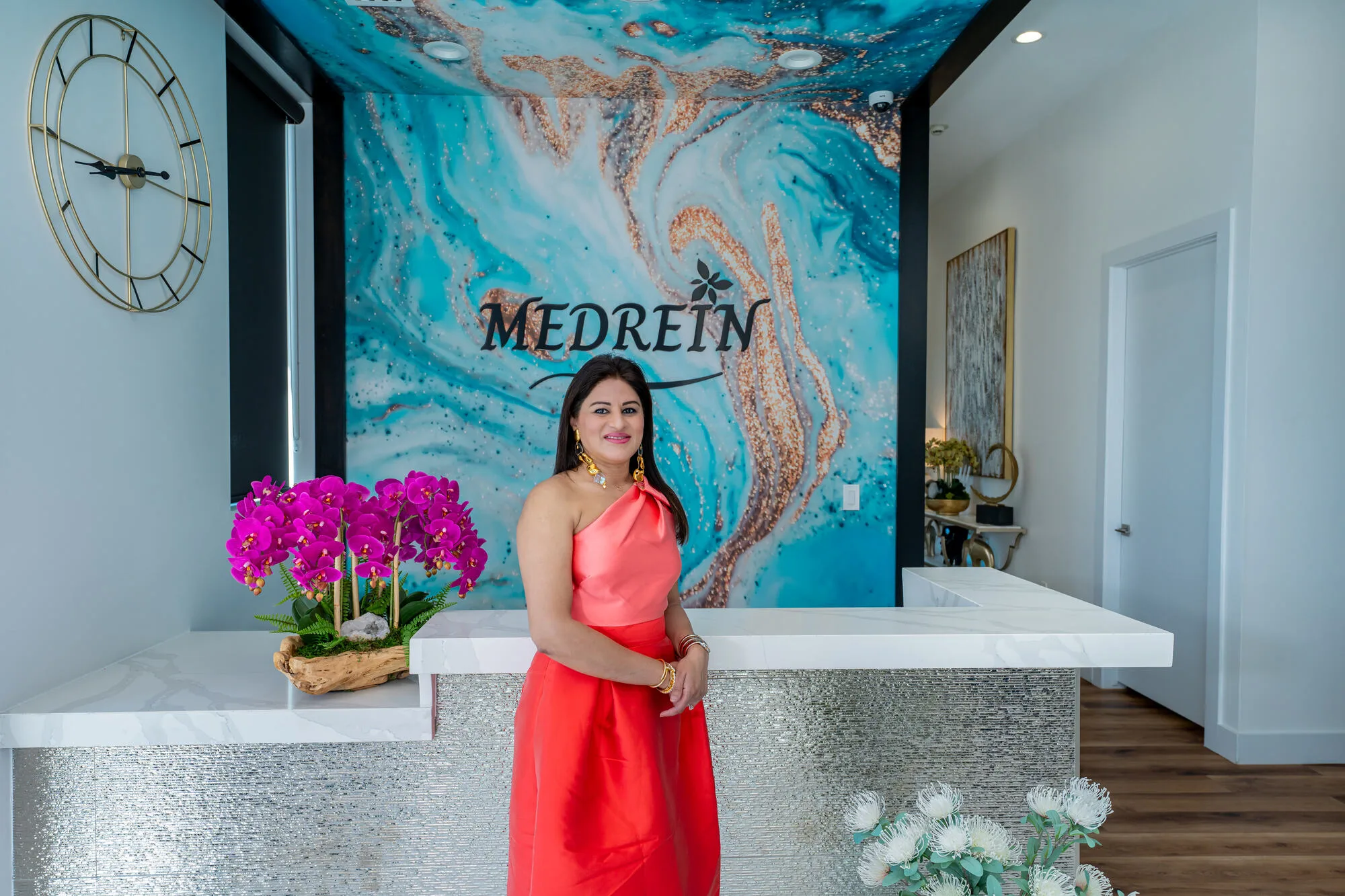 Dr. Haritha Mikkilineni, MD, at the reception desk of the Medrein Health & Aesthetics clinic in Southlake, TX, in front of the Medrein mural
