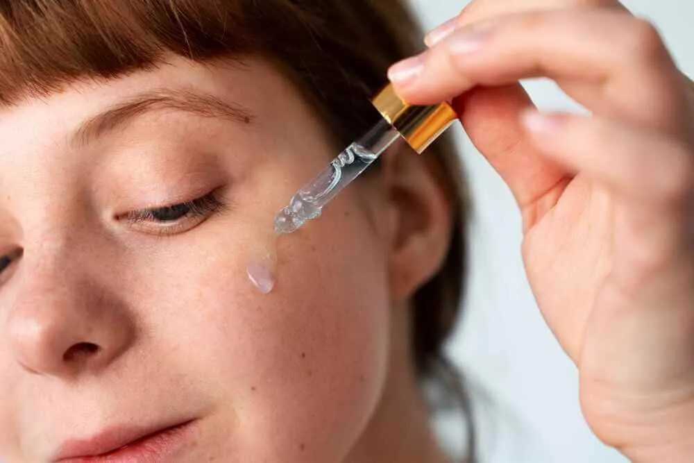 A clear peptide serum being applied to a woman's cheek from a glass dropper, illustrating the topical delivery route for GHK-Cu copper peptide therapy