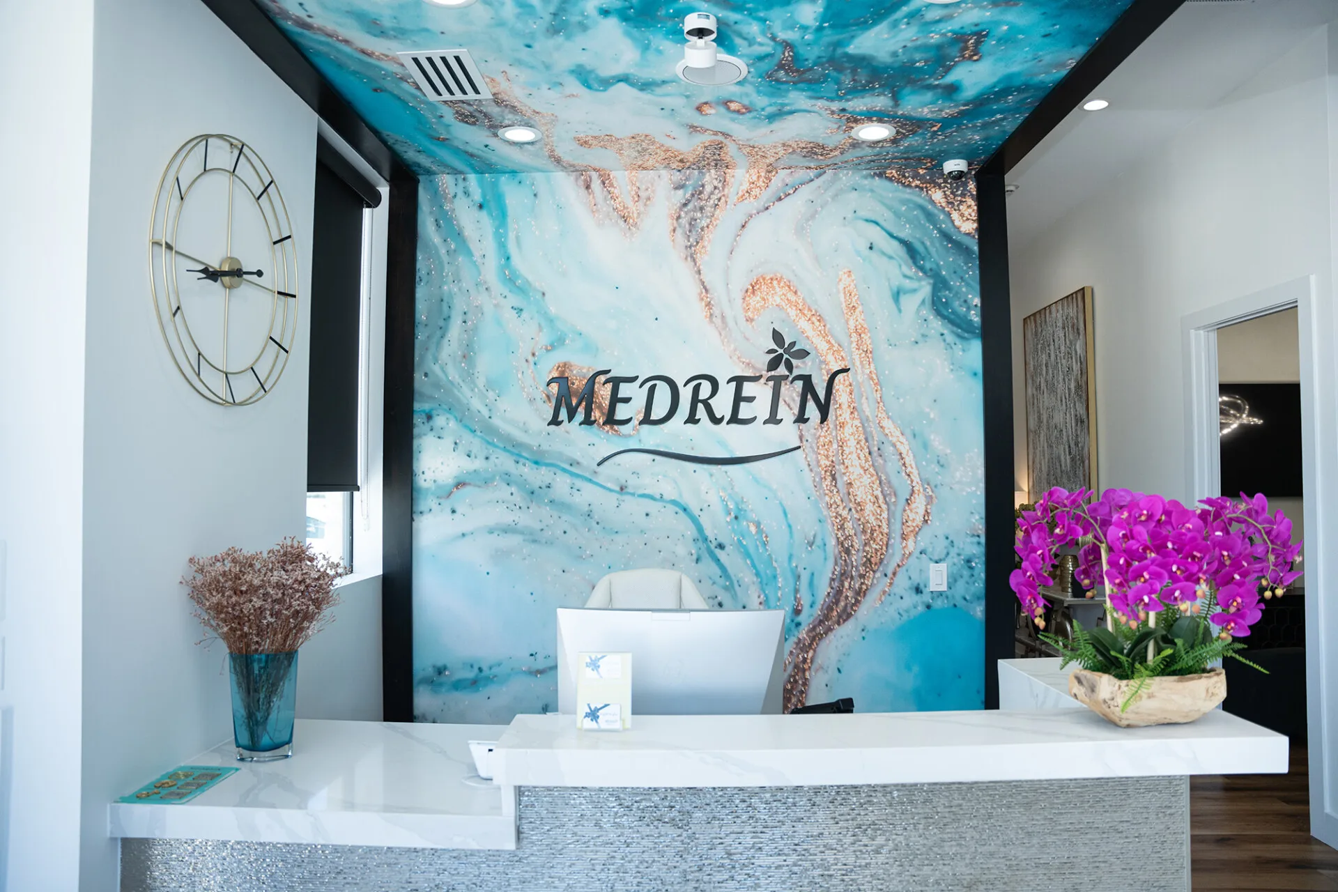The reception desk at Medrein Health in Southlake, TX, beneath the practice's teal and copper resin mural