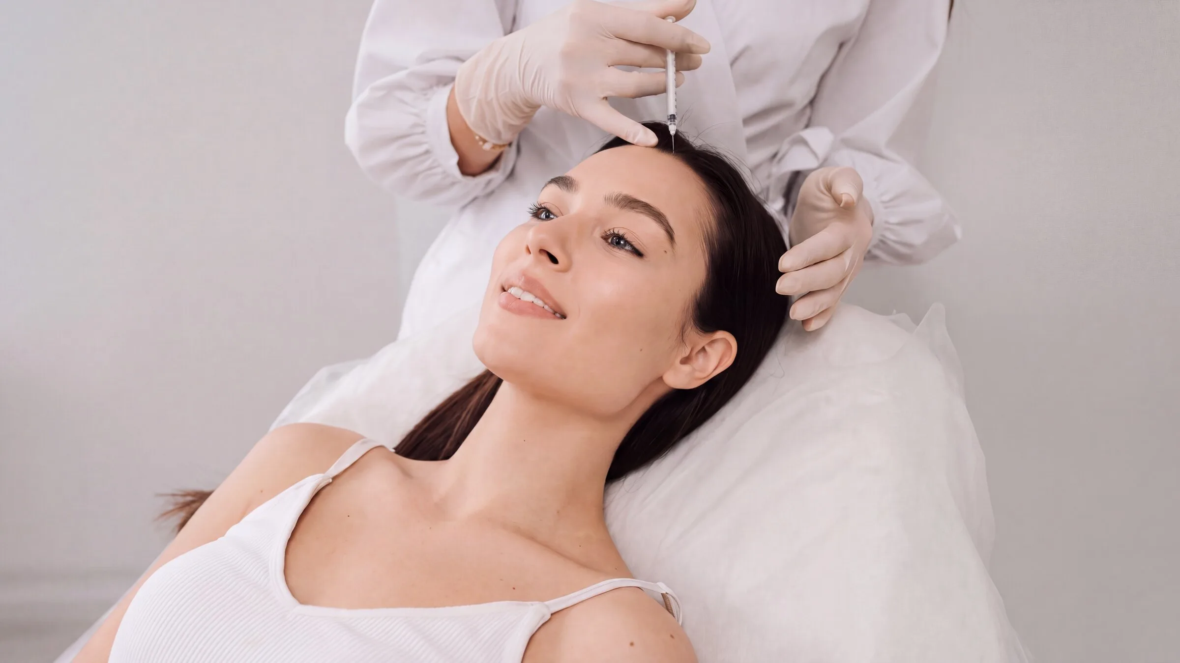 A reclining patient receiving a fine injection at the front hairline from a gloved clinician during a PRP hair restoration session