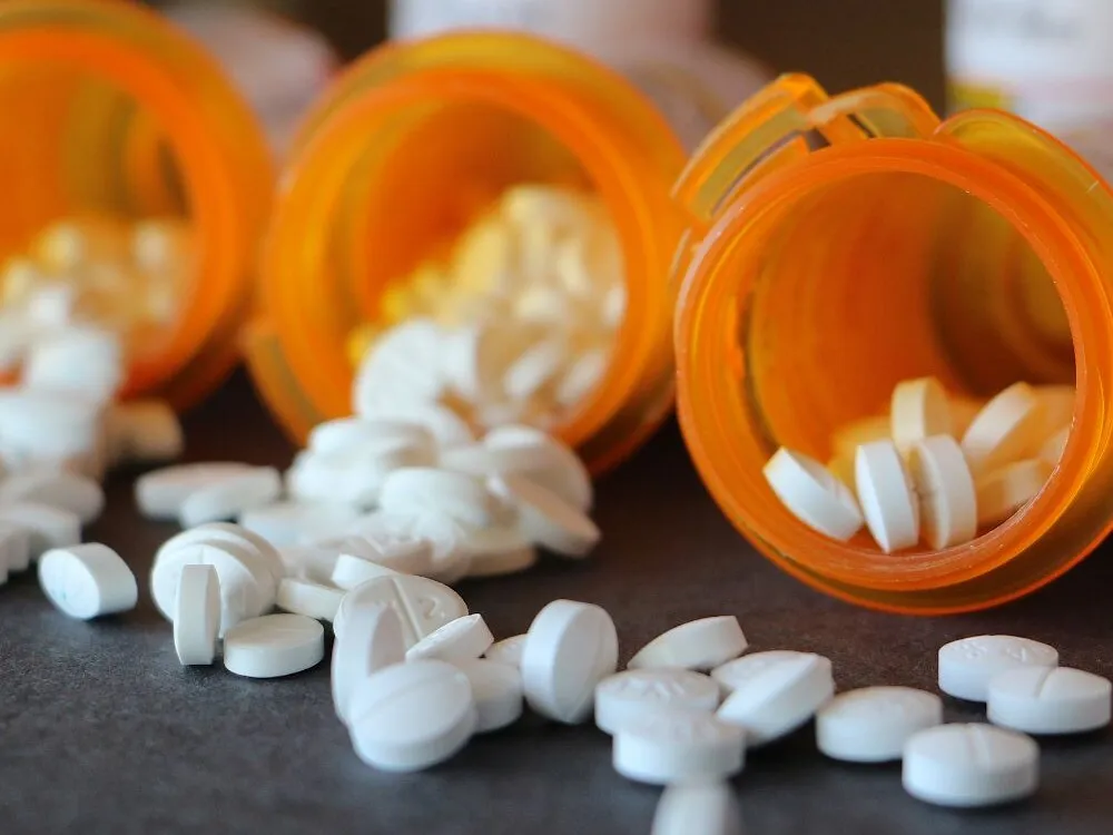 Three tipped amber prescription bottles on a dark counter with white tablets spilling out in front of them