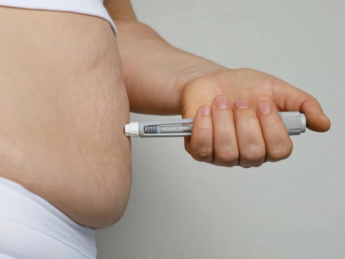An unbranded subcutaneous injection pen held against the abdomen, the route a GLP-1 medication is given by