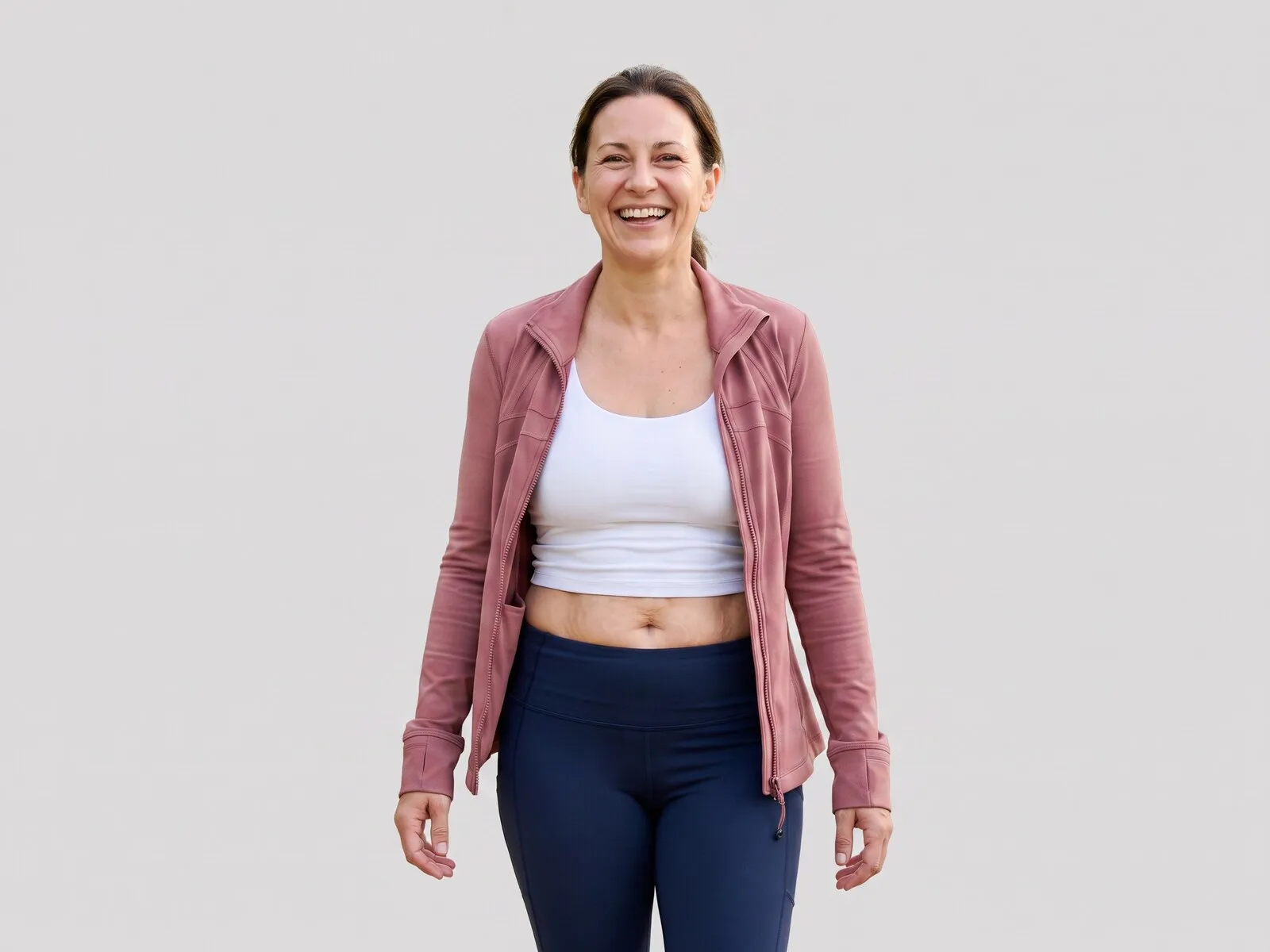 A laughing woman in a pink athletic jacket and navy leggings against a pale grey studio background