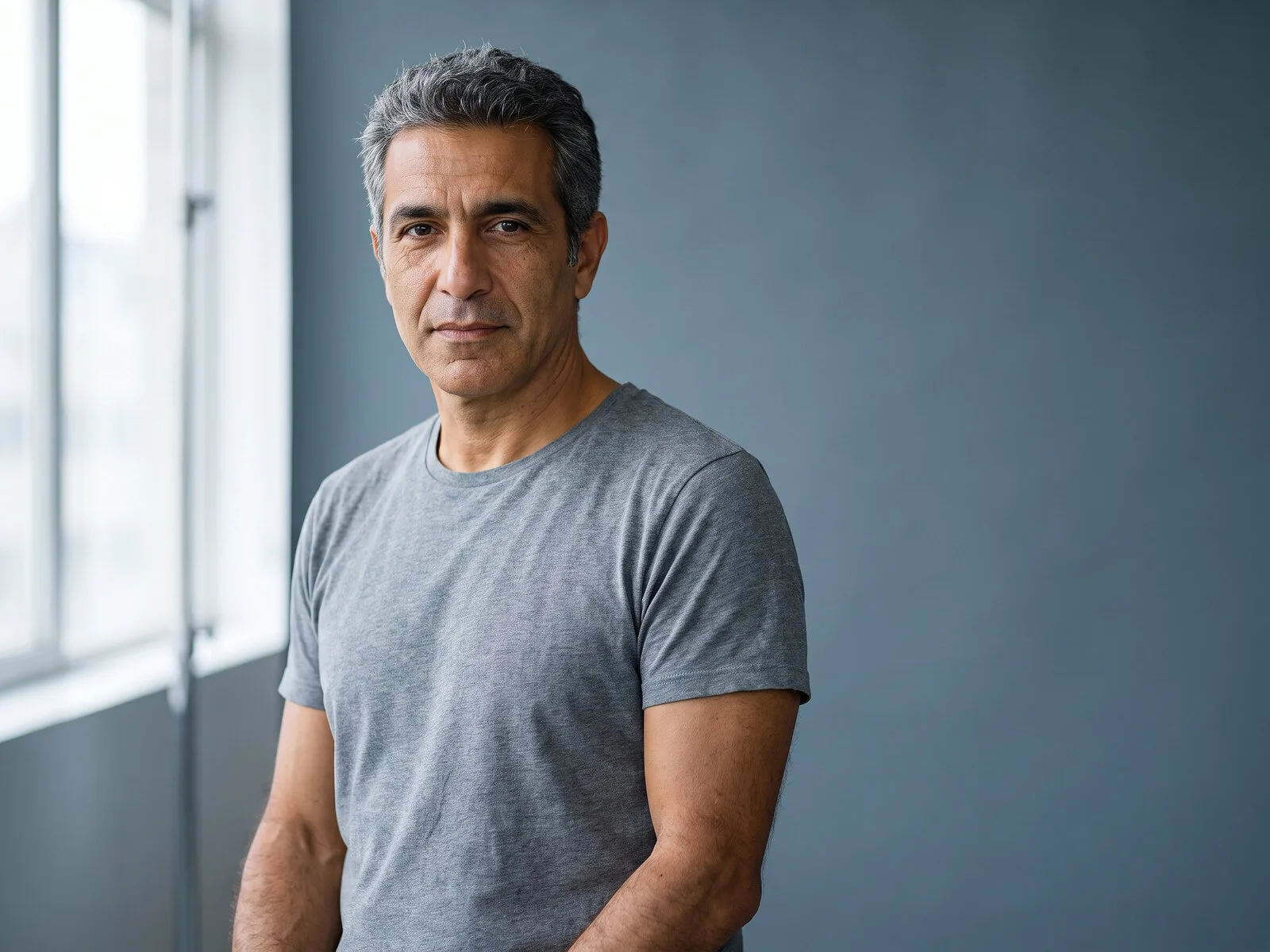 Portrait of a man in his forties standing beside a window, the patient this men's testosterone replacement page is written for