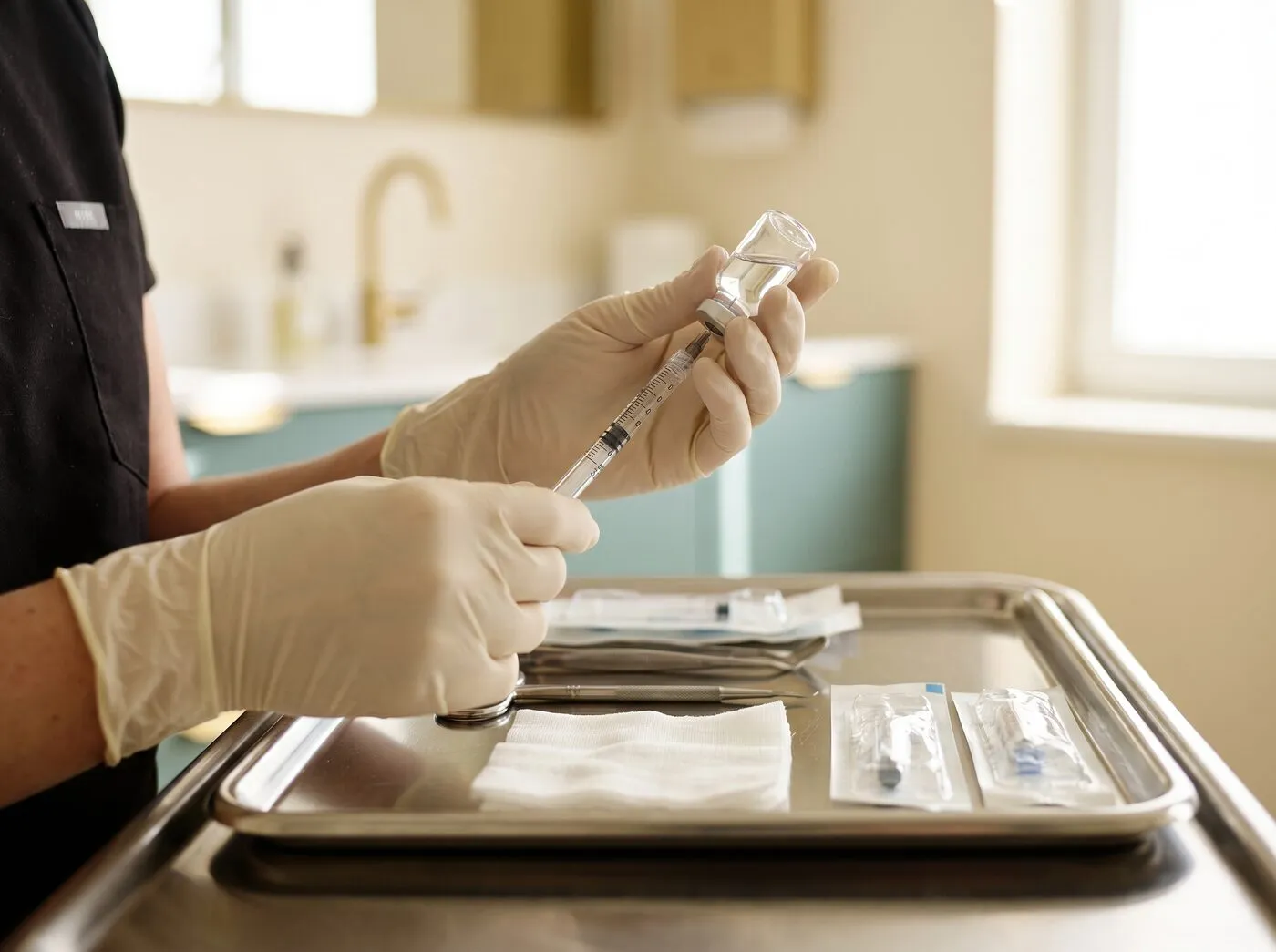 A clinician in gloves preparing a dermal-filler syringe on a sterile tray