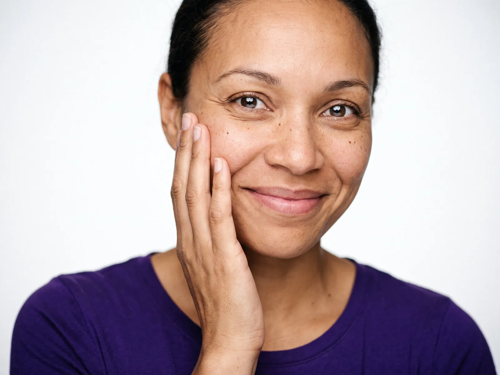 A woman in her forties with her hand resting against her cheek at close range, visible pores and uneven skin tone, the concern an aesthetic consultation at Medrein Health starts from