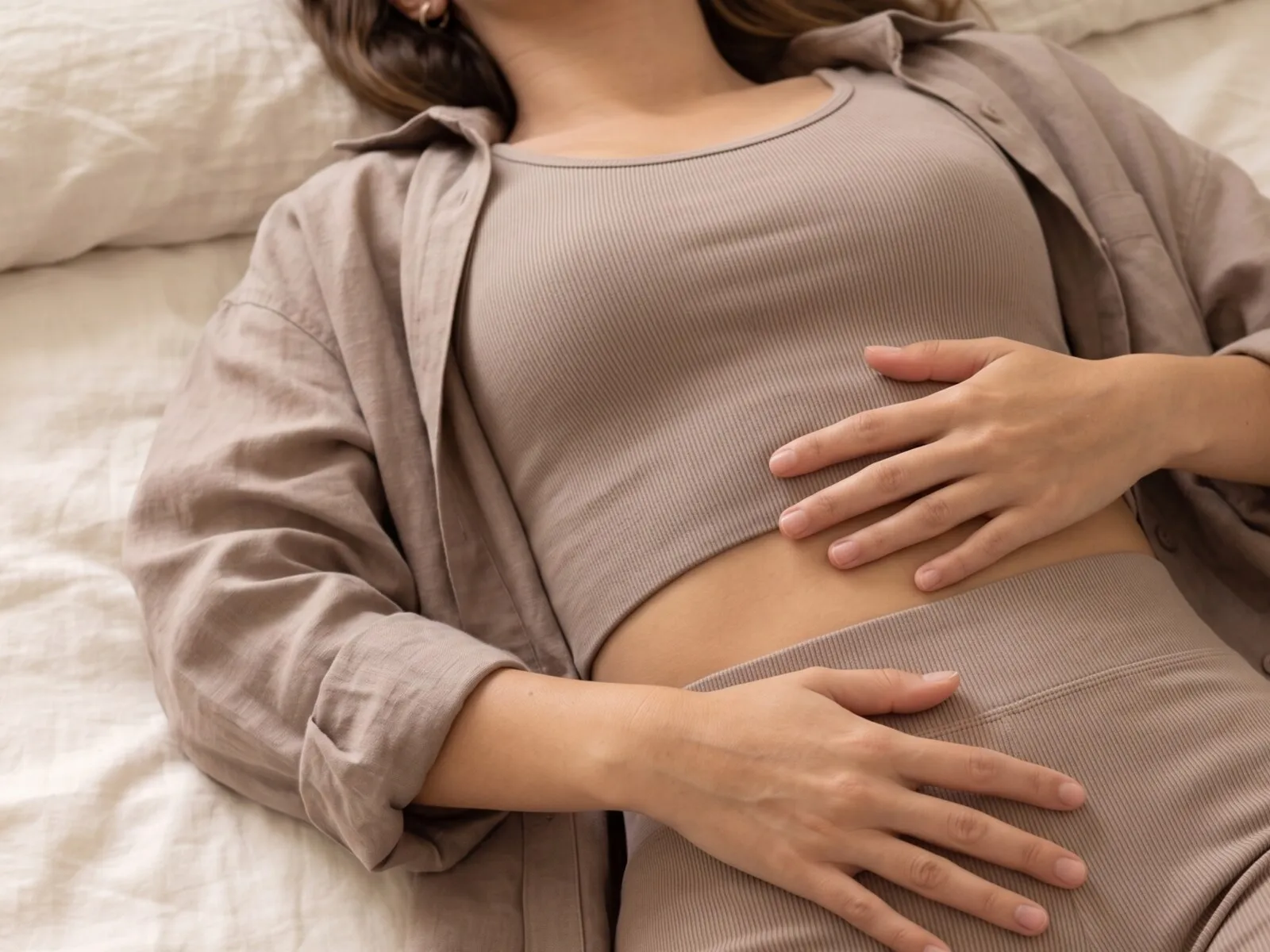 A woman resting on a bed with both of her own hands resting over her lower abdomen