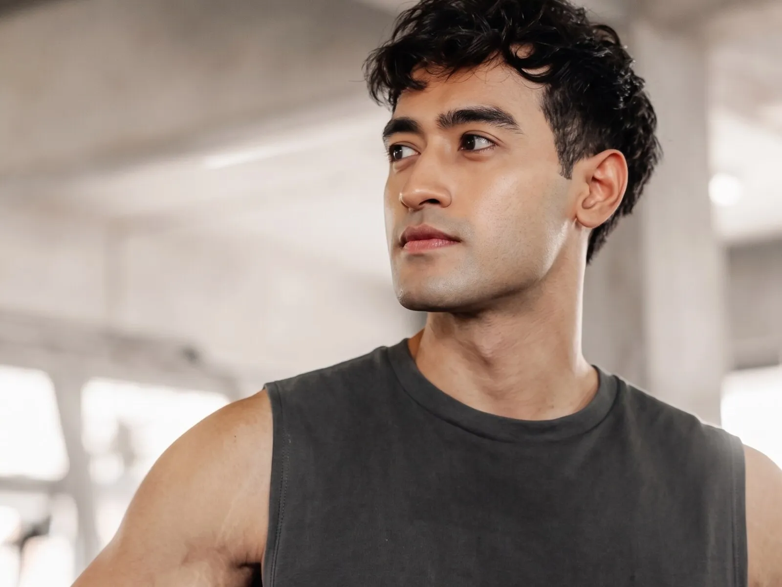 A man in his early thirties in a grey sleeveless top in a gym, his shoulder and upper arm in frame, the muscle GHRH peptides support