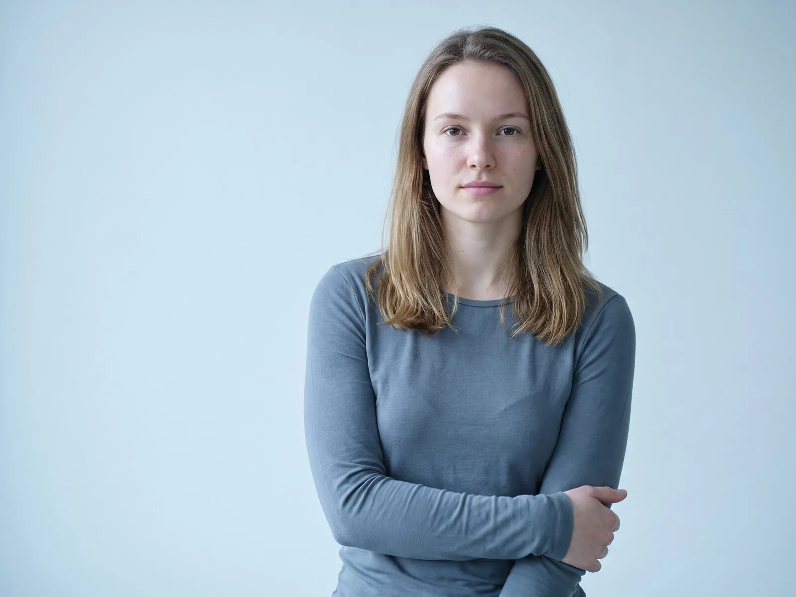 A woman in her late twenties standing with her arms lightly folded against a pale blue-grey ground, the kind of patient who comes to Medrein Health in Southlake, TX about immune support