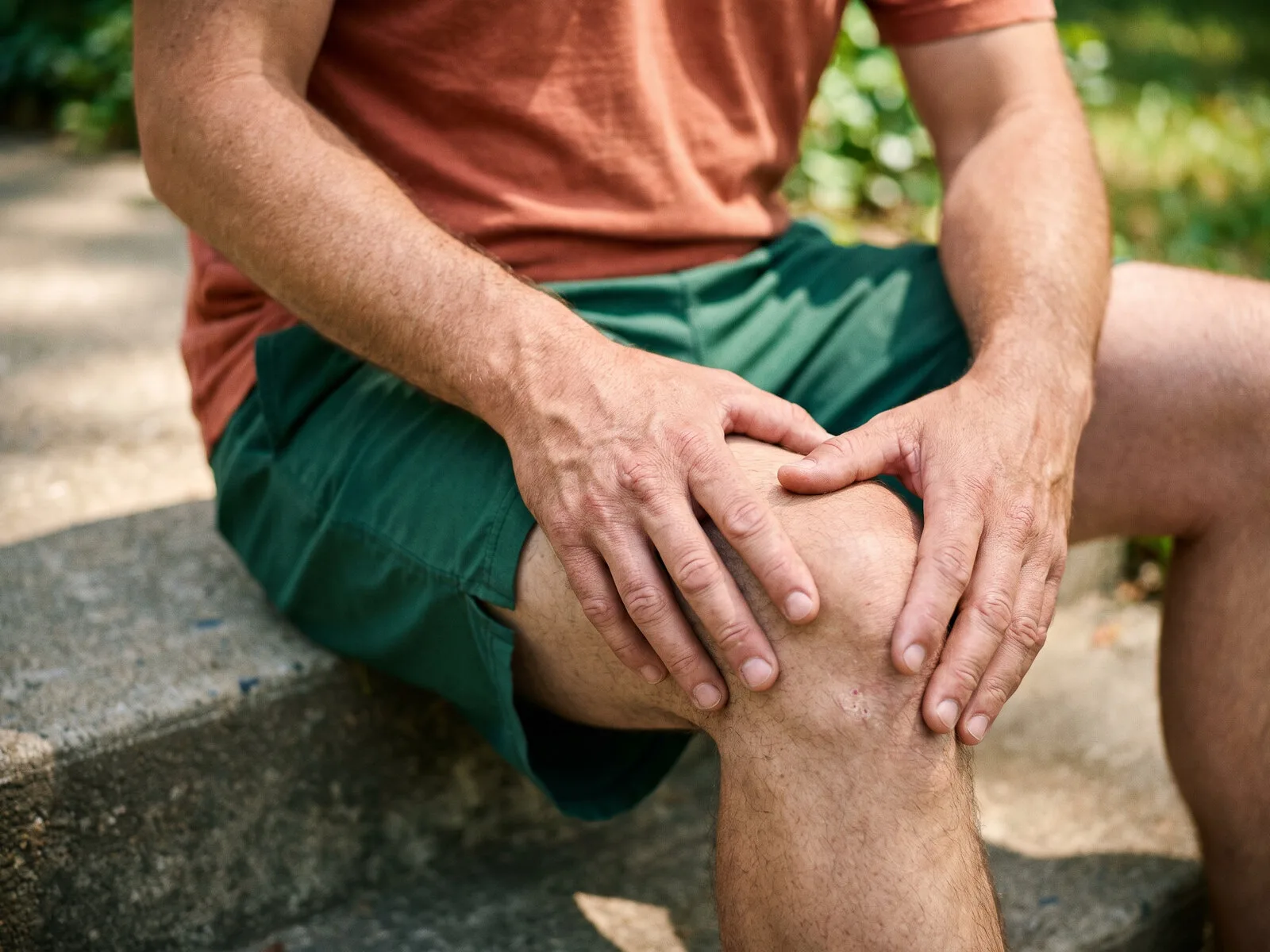 A man resting both hands over his own knee, the kind of joint repair and healing peptides target