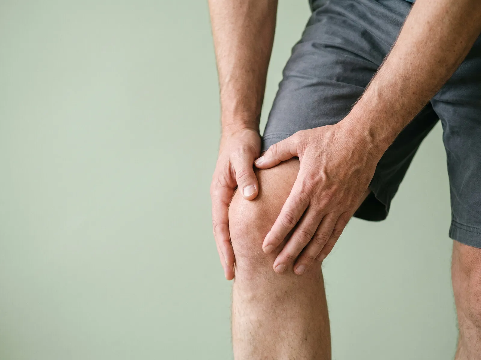 A man resting both hands over his own knee against a soft green ground, the kind of joint repair and healing peptides are prescribed for at Medrein Health in Southlake, TX