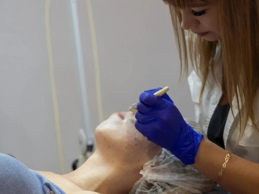 A clinician in a white coat treating pigment on a reclining patient's face during a session at Medrein Health