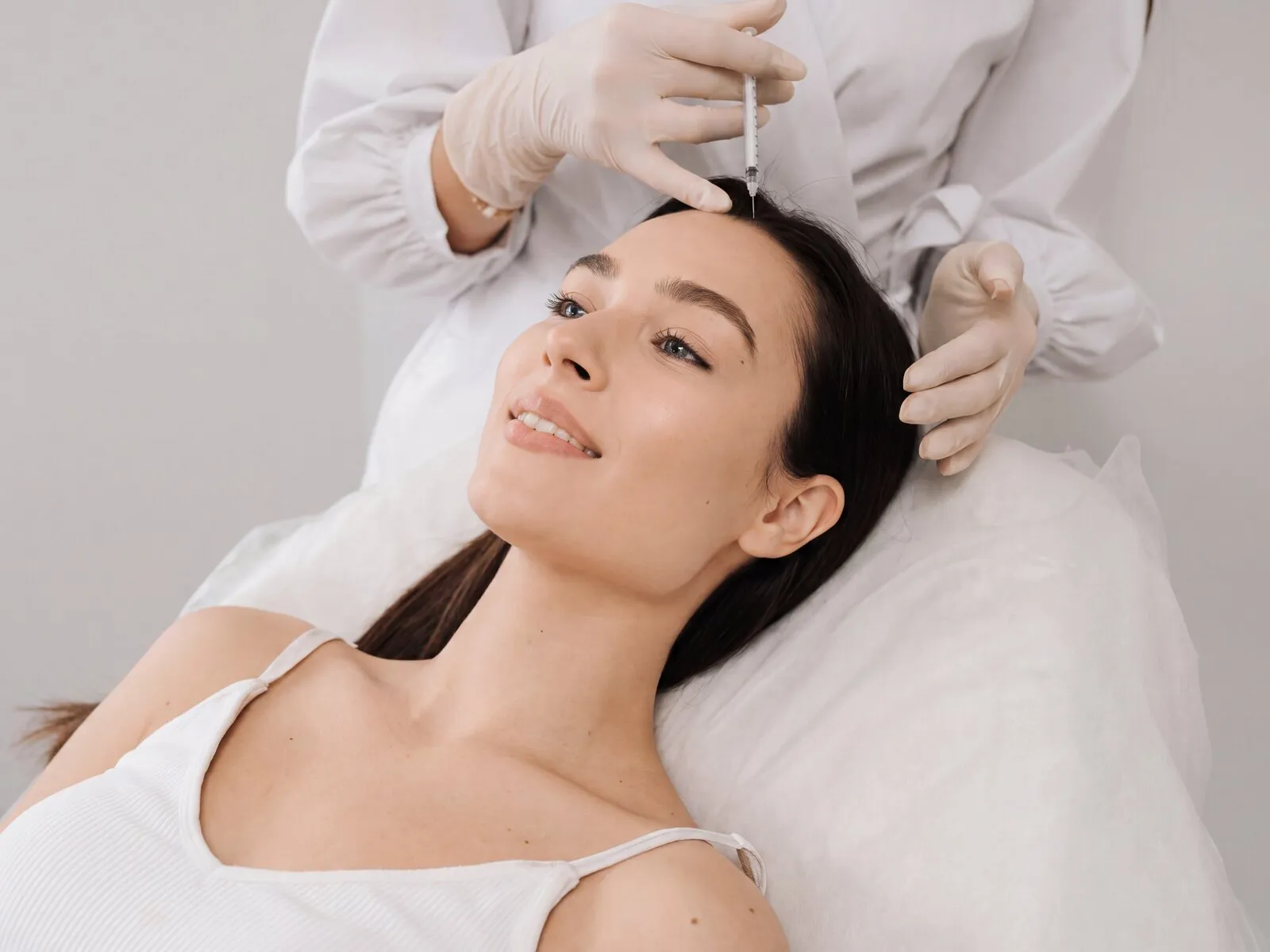 A reclining patient receiving a fine injection at the front hairline, the area PRP/PRF treats